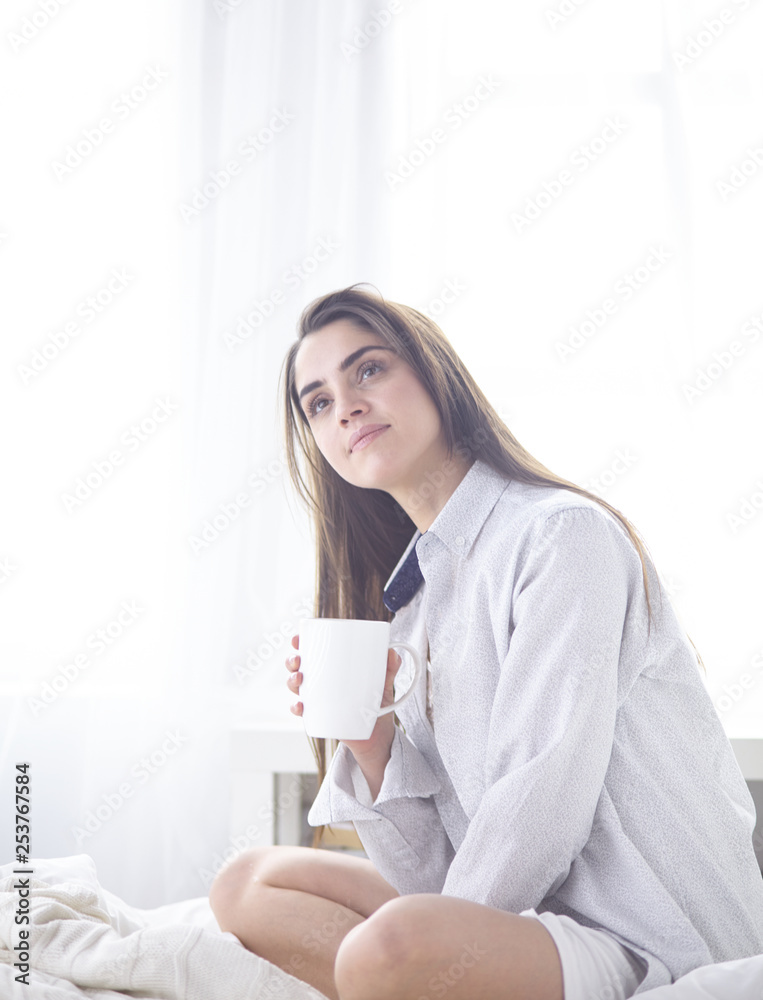 Young beautiful happy brunette woman in black silk dressing gown lying in bed, drinking morning coffee, white cup. Womens day holiday Young beautiful happy brunette woman in black silk dressing gown lying in bed, drinking morning coffee, white cup. Womens day holiday
