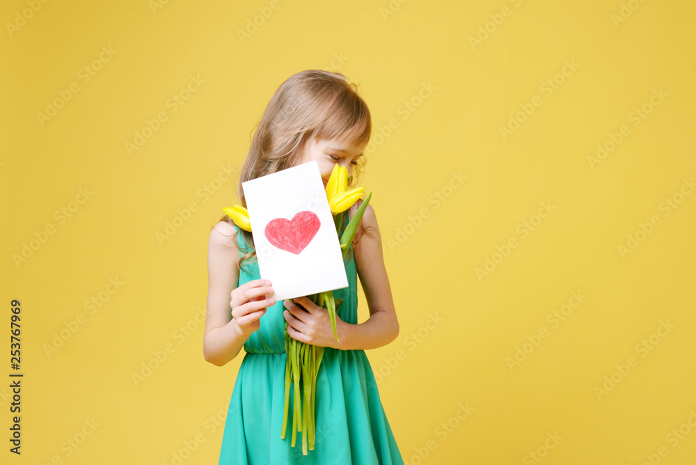 Beautiful baby blonde girl holding yellow tulips and a postcard for a holiday gift. Celebration of international women's day. Concept of holidays, people and beauty. Beautiful baby blonde girl holding yellow tulips and a postcard for a holiday gift. Celebration of international women's day. Concept of holidays, people and beauty.