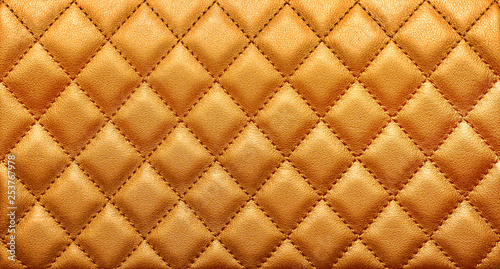 Close-up texture of genuine leather with rhombic stitching. Rich gold color photo