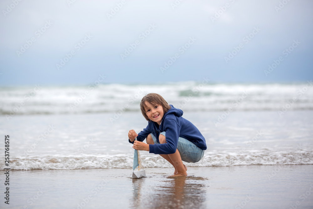 Child plays with sand on beach. Cute preschool boy with toy ship on beach. Stormy seaside sgore and kid playing Child plays with sand on beach. Cute preschool boy with toy ship on beach. Stormy seaside sgore and kid playing