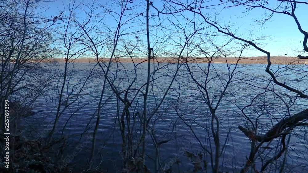 A slow walk alongside a river as it's seen through bushes and tree branches. It's a cloudless sunny afternoon. A slow walk alongside a river as it's seen through bushes and tree branches. It's a cloudless sunny afternoon.