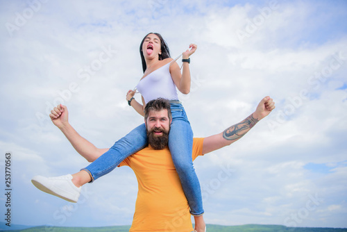 Being on the same wave. Happy couple in love on cloudy sky. Loving couple happy smile having fun. Bearded man piggybacking his girlfriend just for fun. Hipster giving sexy woman a piggyback ride