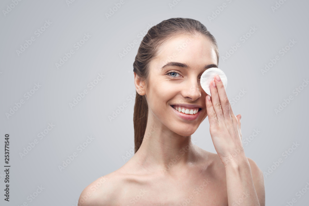 Beauty portraitof a cheerful young topless woman removing face make-up with a cotton pad isolated over white background Beauty portraitof a cheerful young topless woman removing face make-up with a cotton pad isolated over white background