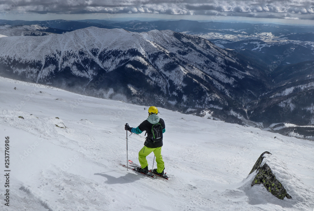 A man skier finding the best track for freeride. A skier looking down to the valley. A yellow helmet. Waiting for right moment. Best choice. Chopok, Low Tatras, Slovakia