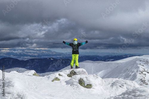 Male Skier is standing on stone and looking down the valley from the top of the mountain. Low Tatras, Chopok. Free ride. A skier is standing at the edge. Cloudy sky. View on High Tatras © Fauren