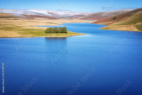 Craig Goch resevoir in Elan Valley Wales with snow topped mountains and trees. Water to supply birmingham reflecting blue sky