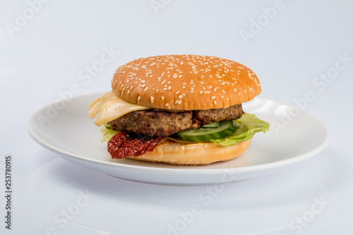 cheeseburger with beef cutlet  bacon  tomatoes and cheese slices  seasoned with sauce and green salad for a restaurant menu on a white isolated background