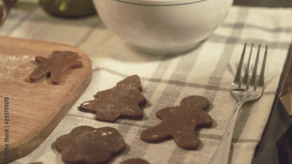 Gingerbread dough cut into various festive Christmas shapes, panning across the kitchen bench