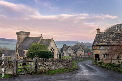 Snowshill church in the Cotswolds gloucestershire with lane leading past a cottage towards red telephone box and country pub