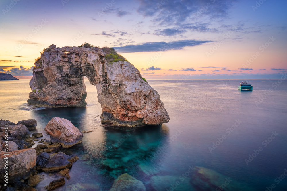 Es Pontas in Mallorca with boat anchored nearby in the Mediterranean sea. Majorca Sunrise with yacht and rock arch near Santanyi.