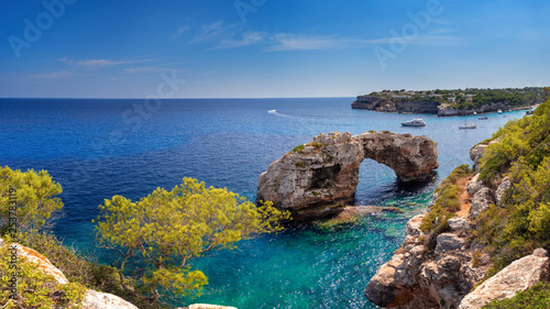 Es Pontas in Mallorca with boat anchored nearby in the Mediterranean sea. Sunny day with yacht and rock arch near Santanyi Majorca