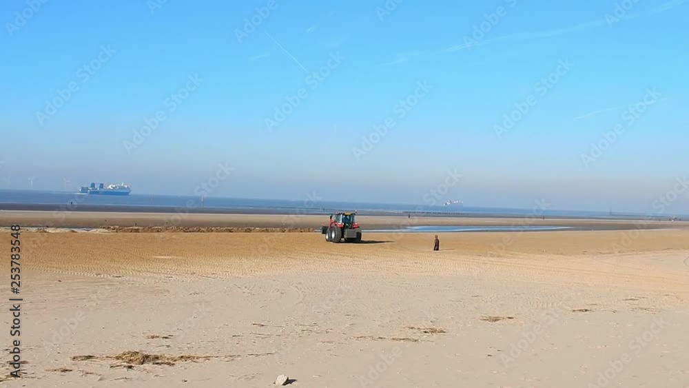 Wide view of red tractor relocating sand back to beach. Boat in background on ocean waters. Wide view of red tractor relocating sand back to beach. Boat in background on ocean waters.