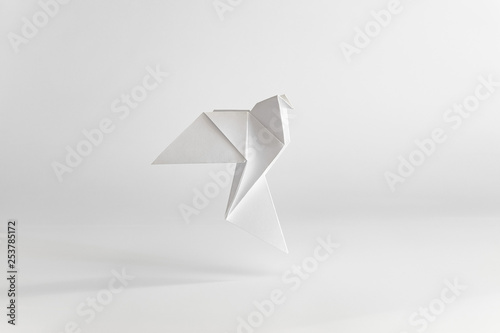 Origami dove made of white paper on white background. Minimal concept.