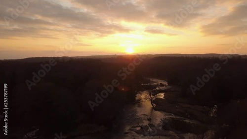 Reversing drone footage over a river through a forest at sunset golden hour. photo