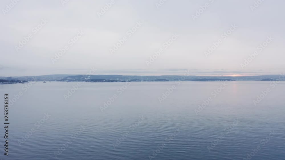 Flight over calm morning Nordic sea with mountains on background during sunrise - Oslofjord, Norway, winter Flight over calm morning Nordic sea with mountains on background during sunrise - Oslofjord, Norway, winter