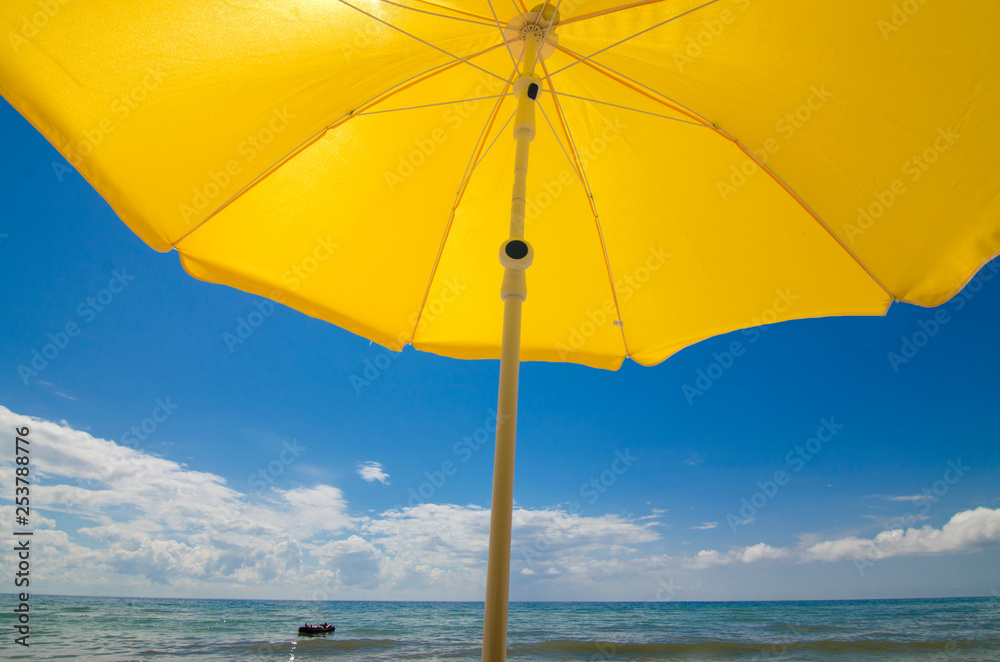 Sun umbrella on a sandy seashore on a hot July day. People are swimming in the sea.