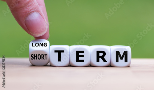 Hand turns a dice and changes the expression "SHORT TERM" to "LONG TERM" (or vice versa).