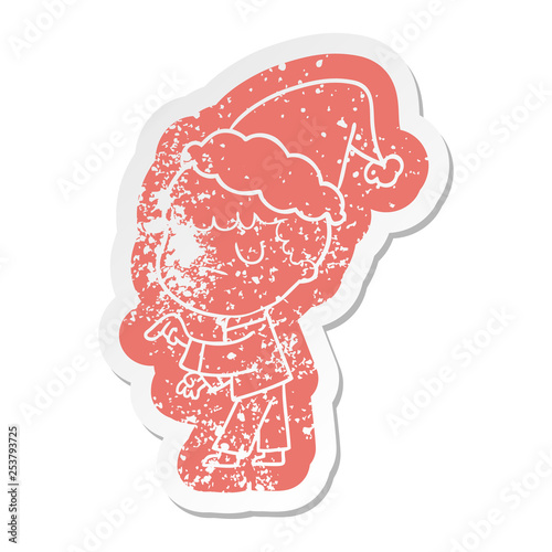 cartoon distressed sticker of a grumpy boy wearing santa hat