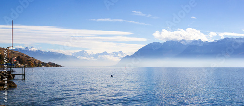 Panorama of Lake Leman or Lake of Geneva with morning mist over the water surface. At the background are the snow-covered Alps, at the right side is mountains in France.