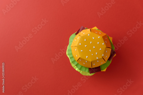 Fototapeta Paper cheeseburger with beef, cheese, tomato, lettuce, onion, bacon and sauce on red background. Copy space. Creative or art food concept