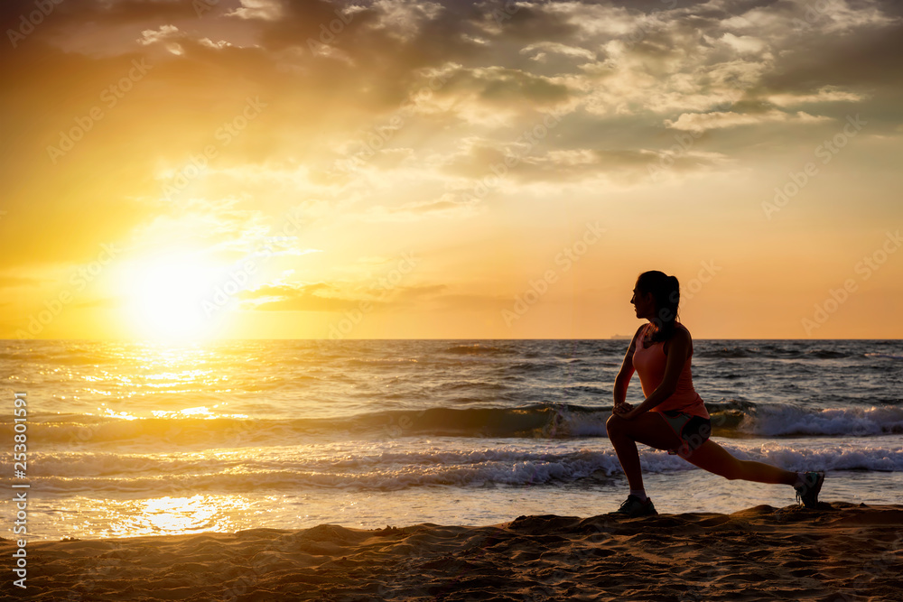 Silhouette einer sportlichen Frau bei Stretching nach ihrem Training am Strand bei Sonnenuntergang