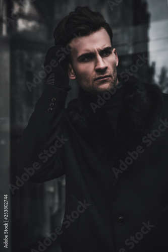 Fashion man model portrait on city street. Young guy posing near shops. Wearing in black coat and gloves. Elegant style © Yevhen