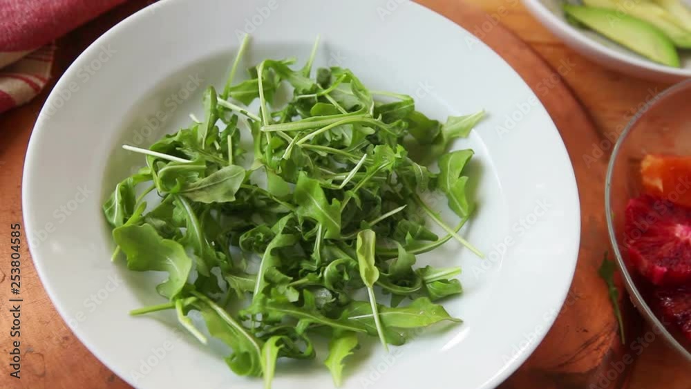 A woman adds fresh orange rounds and avocado slices to baby lettuces A woman adds fresh orange rounds and avocado slices to baby lettuces