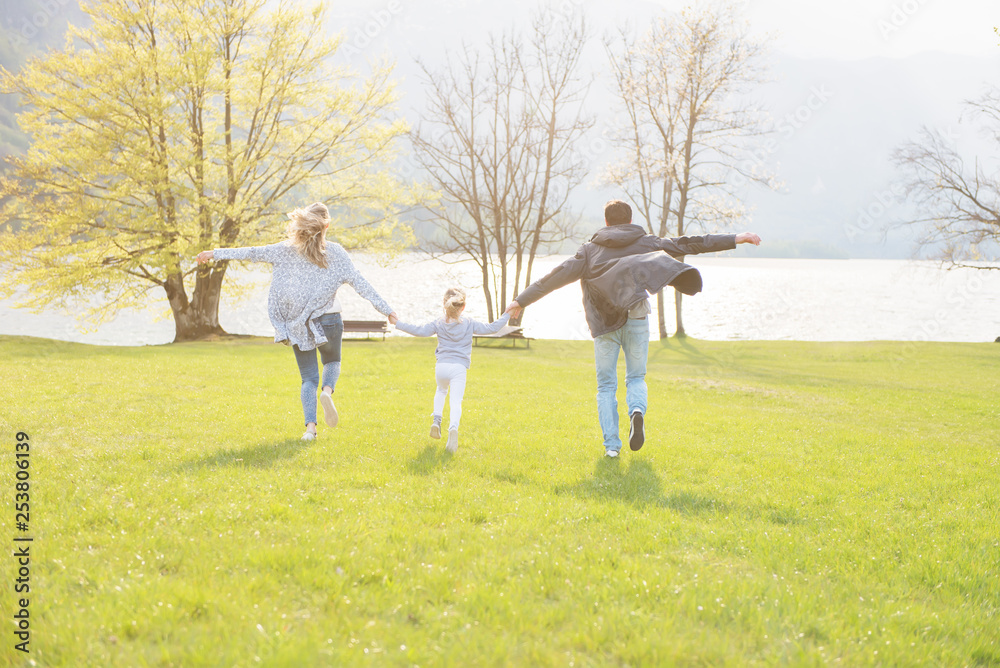Happy father, mother and little girl running alongside lake and enjoying on a beautiful sunny day. Happy father, mother and little girl running alongside lake and enjoying on a beautiful sunny day.