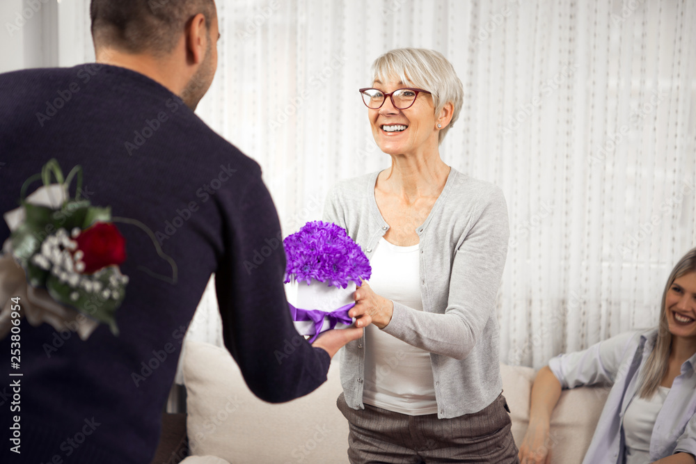 Handsome young man giving a beautiful purple flowers to mother of his girlfriend. Handsome young man giving a beautiful purple flowers to mother of his girlfriend.
