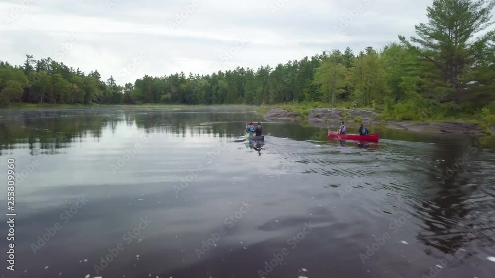 Low flying drone shot follow a two canoes rowing across a lake Low flying drone shot follow a two canoes rowing across a lake