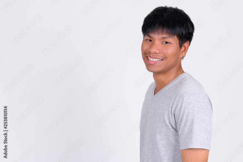 Profile view of happy young Asian man smiling and looking at camera Profile view of happy young Asian man smiling and looking at camera