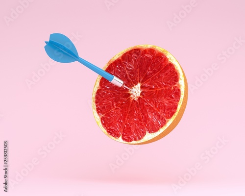 Grapefruit slice, fruit with circular target marked and blue dart on pastel pink background.minimal idea food and fruit concept.Idea creative to produce work and advertising marketing communications