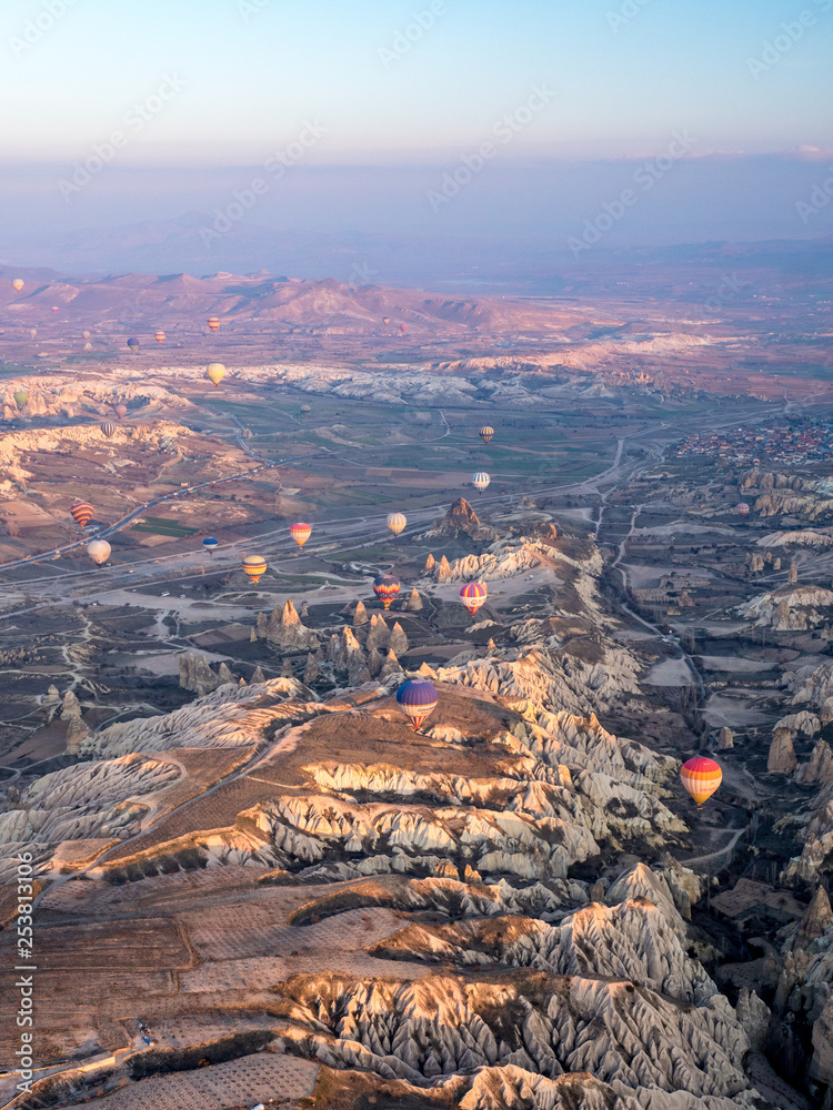 Colorful hot air balloons above Turkish National Park in Goreme. Panorama of Cappadocia landscape - multi colored balloons flying over mountain valley of ancient cave town Uchisar. March, 2019