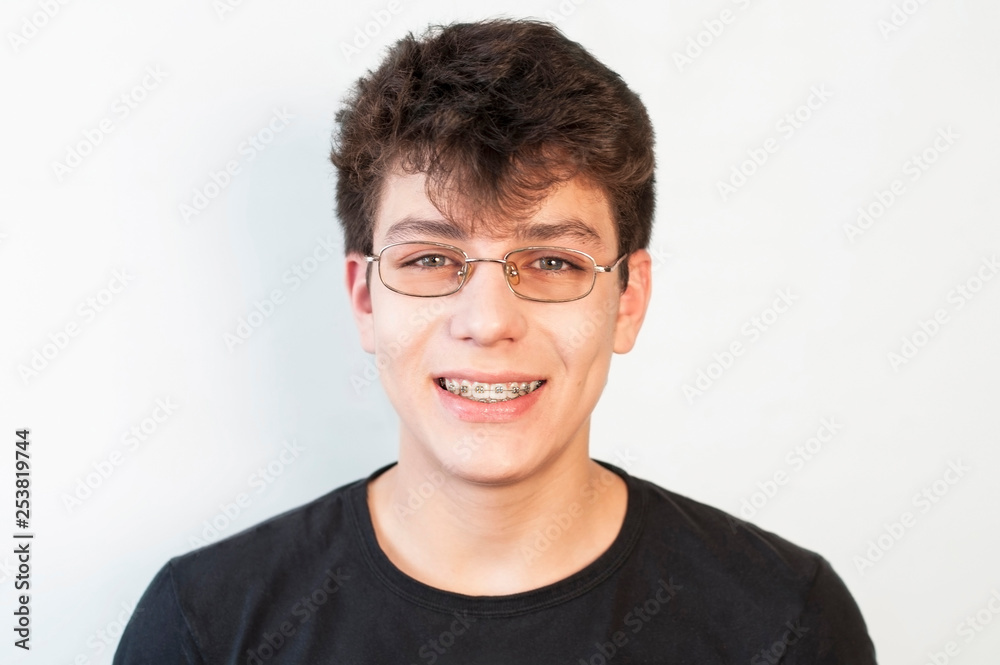 The teenager in glasses sincerely smiles on a light background and on the teeth has braces The teenager in glasses sincerely smiles on a light background and on the teeth has braces