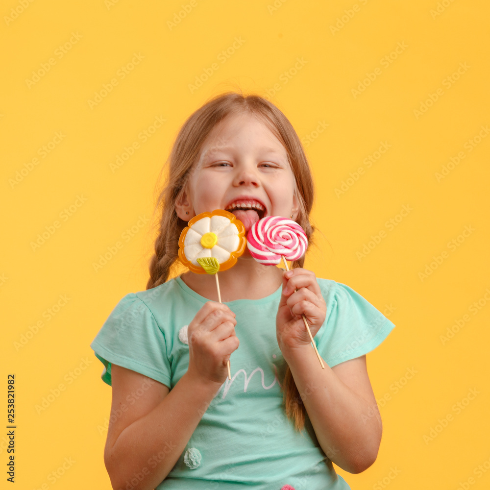 Cute little girl licks candy and laughs in the studio on a yellow background Cute little girl licks candy and laughs in the studio on a yellow background