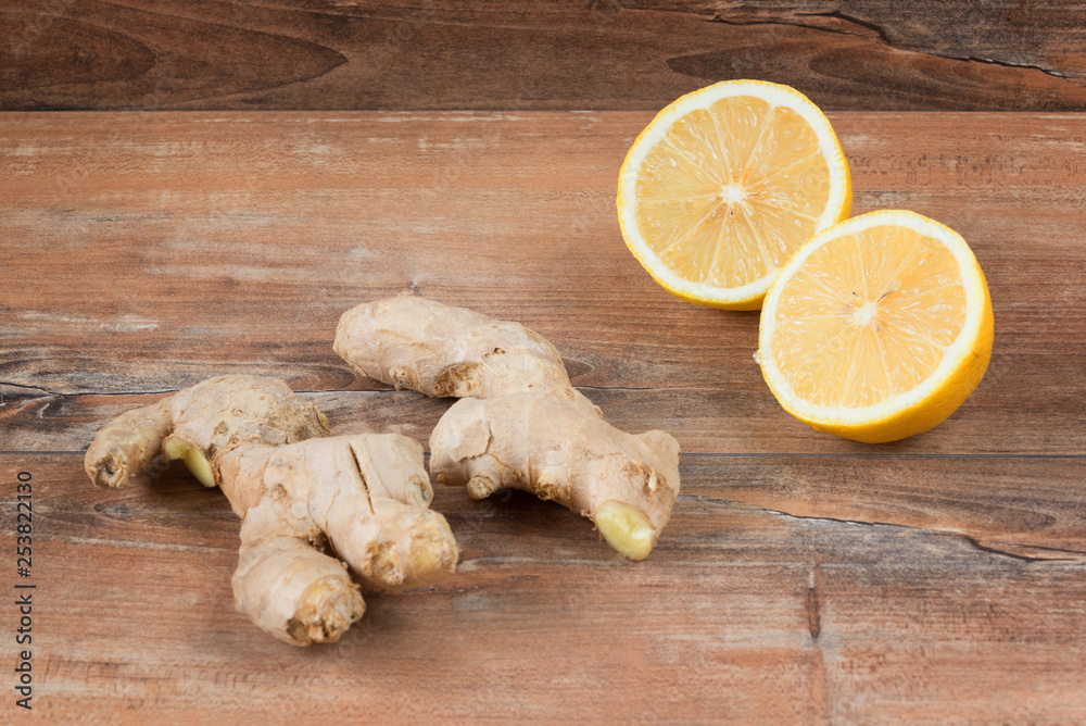 Closeup image of ingredients for natural cold or flu remedy includes ginger and lemon on a brown wooden background. Selective focus on front slice of ginger.