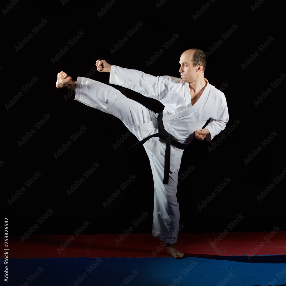 Black belt athlete doing formal karate exercises on red and blue tatami
