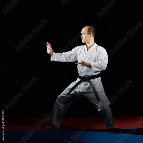 Black belt athlete performs formal karate exercises on red and blue tatami