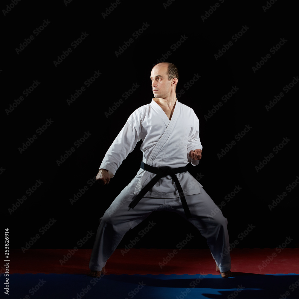With a black belt athlete trains formal karate exercises on red and blue tatami