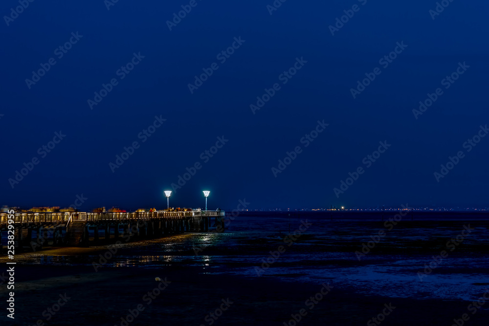 Night time image of a jetty at low tide with people blurred. Andernos les Bains, Arcachon Bay, France
