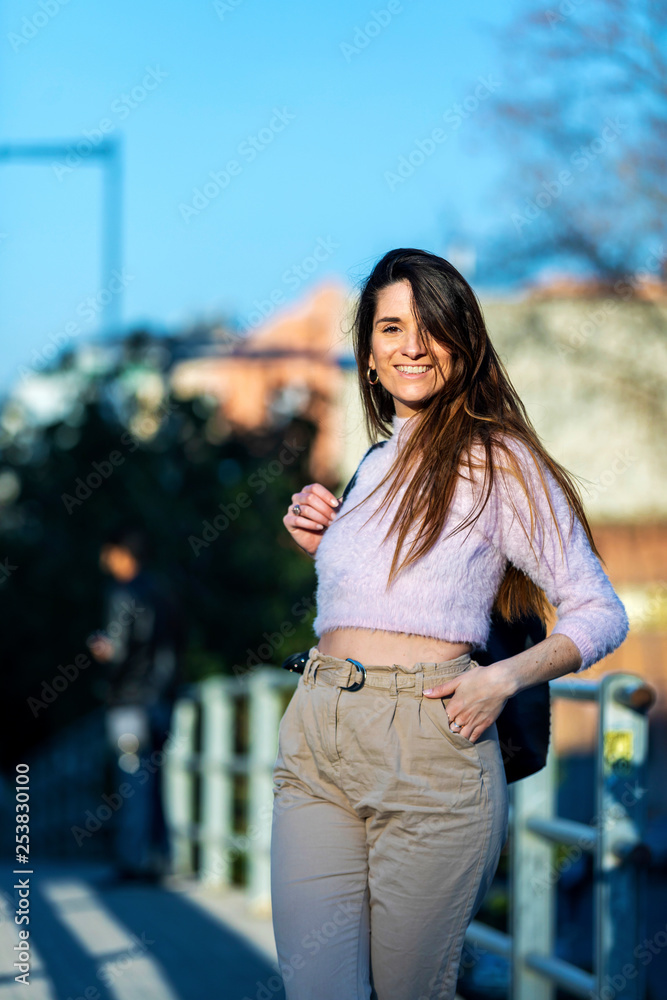 Front view of smiling beautiful young woman hand on pocket standing in the street while looking away in a sunny day