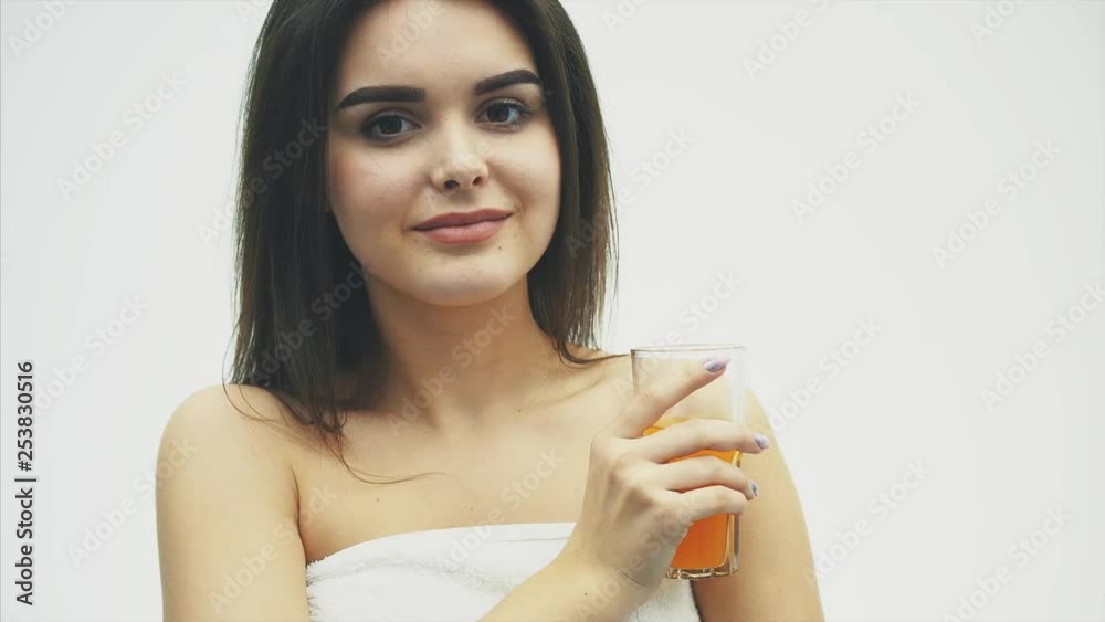 The young beautiful woman drinks sweet orange juice from a transparent glass with a smile, over a white background. With beautiful black long hair. The young beautiful woman drinks sweet orange juice from a transparent glass with a smile, over a white background. With beautiful black long hair.