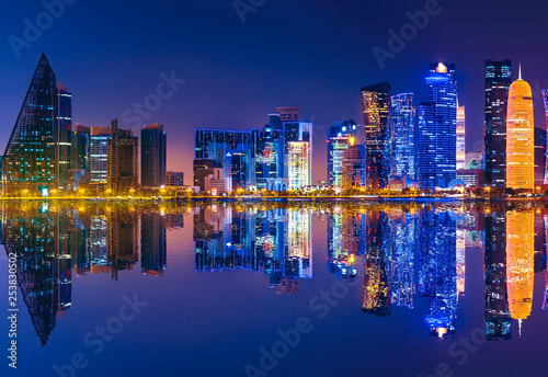 Doha West Bay skyline lighting by night reflecting in Doha Bay. Modern skyscrapers of Doha in Qatar, Middle East, Arabian Peninsula in Persian Gulf. Night urban scene.