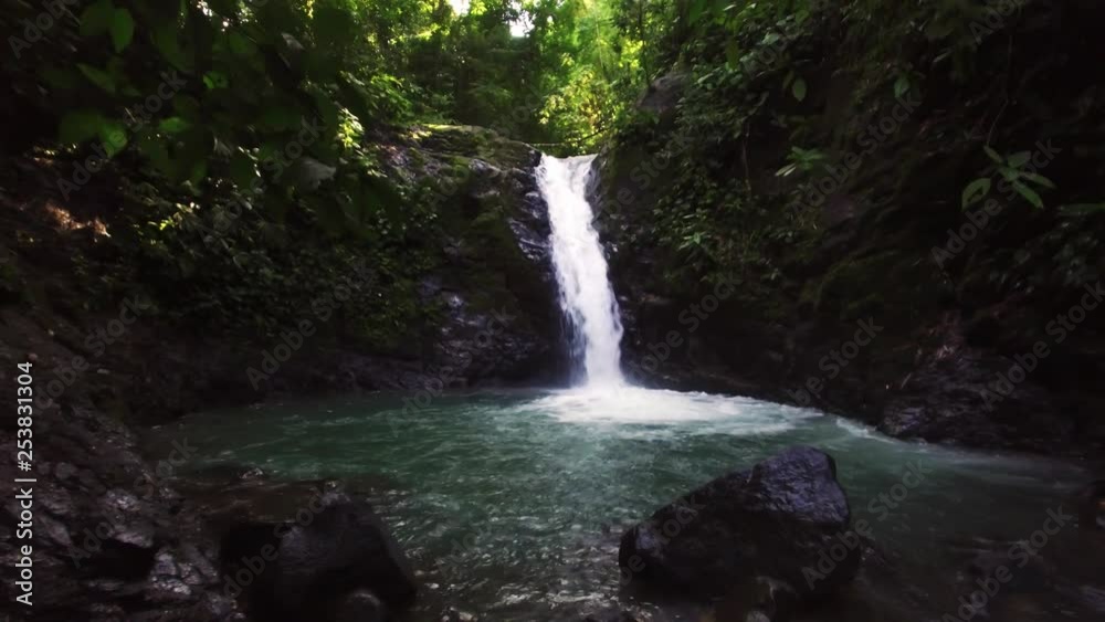 Wide shot through shadowy woodland foliage to view secluded tranquil waterfall flowing into bright turquoise blue pool below. Wide shot through shadowy woodland foliage to view secluded tranquil waterfall flowing into bright turquoise blue pool below.