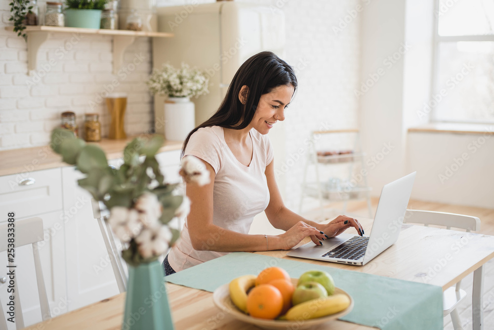 Young beautiful woman using laptop in kitchen sitting at the table
