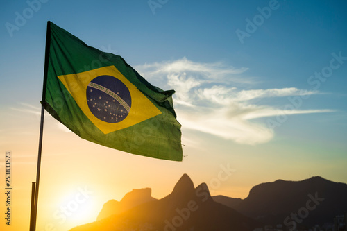 Brazilian flag waving backlit in front of the golden sunset mountain skyline at Ipanema Beach in Rio de Janeiro, Brazil photo