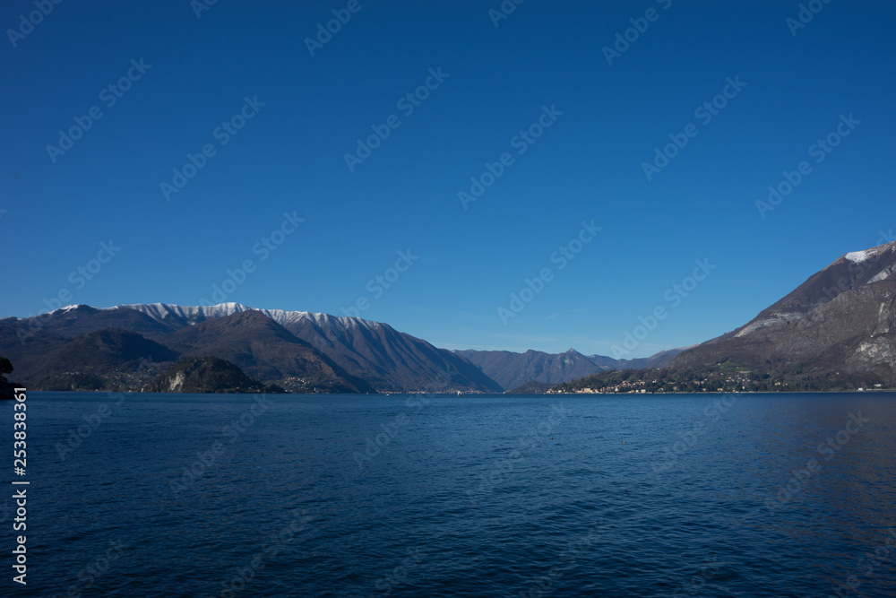 Italy, Menaggio, Lake Como, a large body of water with a mountain in the background Italy, Menaggio, Lake Como, a large body of water with a mountain in the background