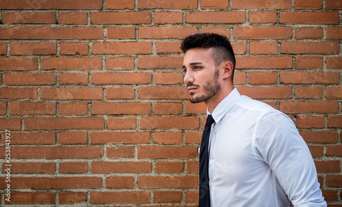 Attractive young man standing against brick wall, looking away. Half body shot © theartofphoto