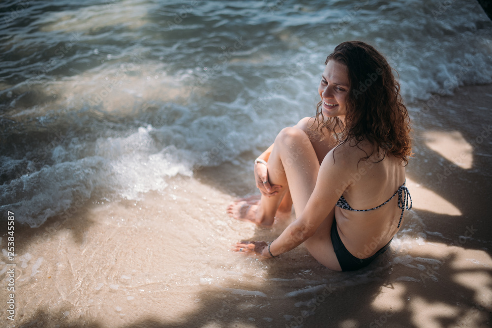 Young slim girl sitting in the shade of a tree in the sea waves on the coast of a tropical island Young slim girl sitting in the shade of a tree in the sea waves on the coast of a tropical island