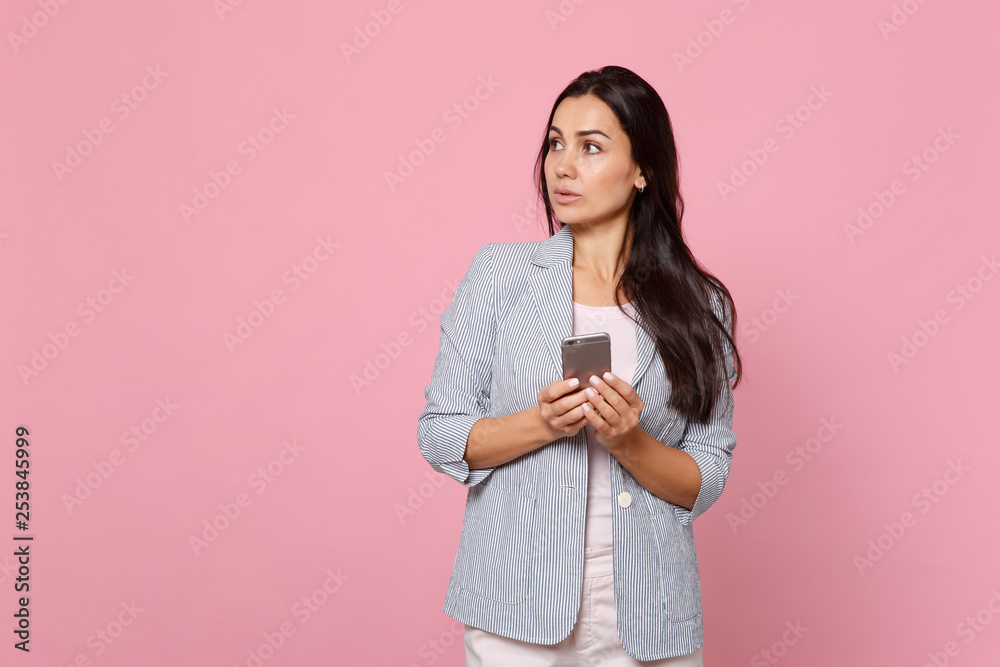 Pensive young woman in striped jacket looking aside using mobile phone, typing sms message isolated on pink pastel background in studio. People sincere emotions, lifestyle concept. Mock up copy space. Pensive young woman in striped jacket looking aside using mobile phone, typing sms message isolated on pink pastel background in studio. People sincere emotions, lifestyle concept. Mock up copy space.